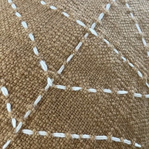 May include: Close-up of a brown fabric with white stitching in a diamond pattern.