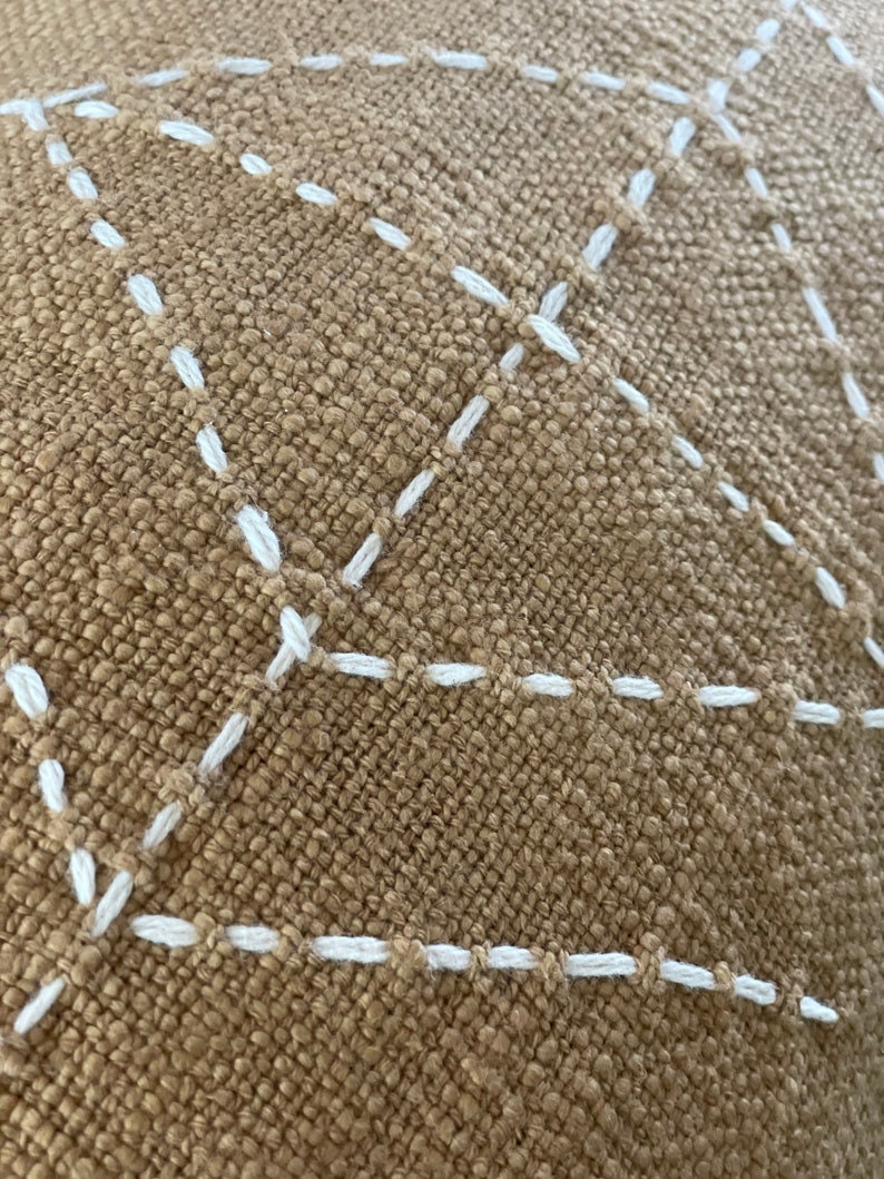 May include: Close-up of a brown fabric with white stitching in a diamond pattern.