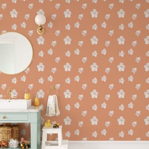 May include: A bathroom with a peach-colored wall covered in a white floral pattern wallpaper. A round mirror hangs on the wall above a white sink and a light blue cabinet. A white stool with a rubber duck toy sits in the corner.