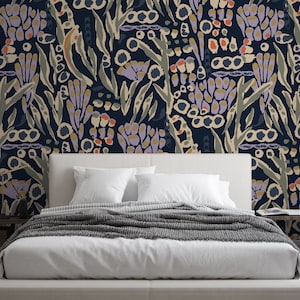May include: A white bed with a gray blanket and two white pillows in front of a dark blue wall with a floral pattern. The pattern features abstract shapes in shades of purple, orange, yellow, and green.