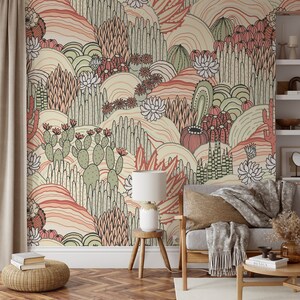 May include: A colorful wallpaper mural featuring a desert landscape with cacti, succulents, and flowers in shades of pink, green, and beige. The mural is displayed in a living room setting with a couch, a lamp, and a side table.