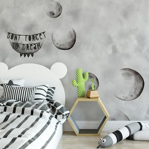 May include: A white bed with a black and white striped comforter and pillows. The headboard is shaped like a bear's head. There is a small hexagonal side table with a green cactus and a small plant on it. The wall behind the bed is gray with a watercolor design of moons and the text "Don't forget to dream".