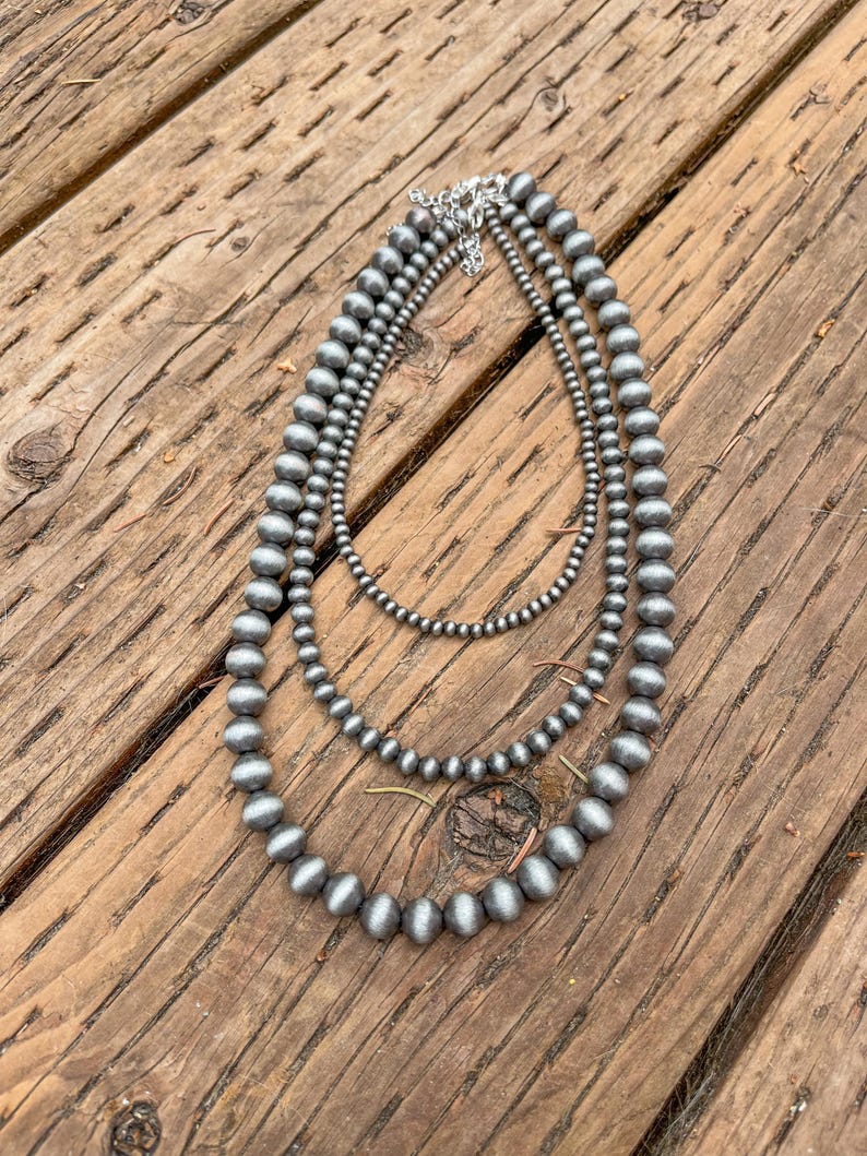 May include: A layered necklace with three strands of silver-toned beads. The beads are round and have a smooth, matte finish.