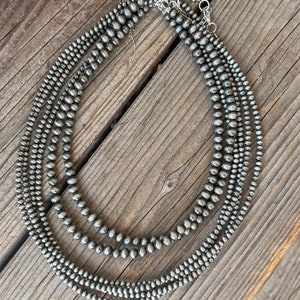 May include: A layered necklace made of five strands of gray, round, smooth beads. The necklace is made of a silver-toned metal.
