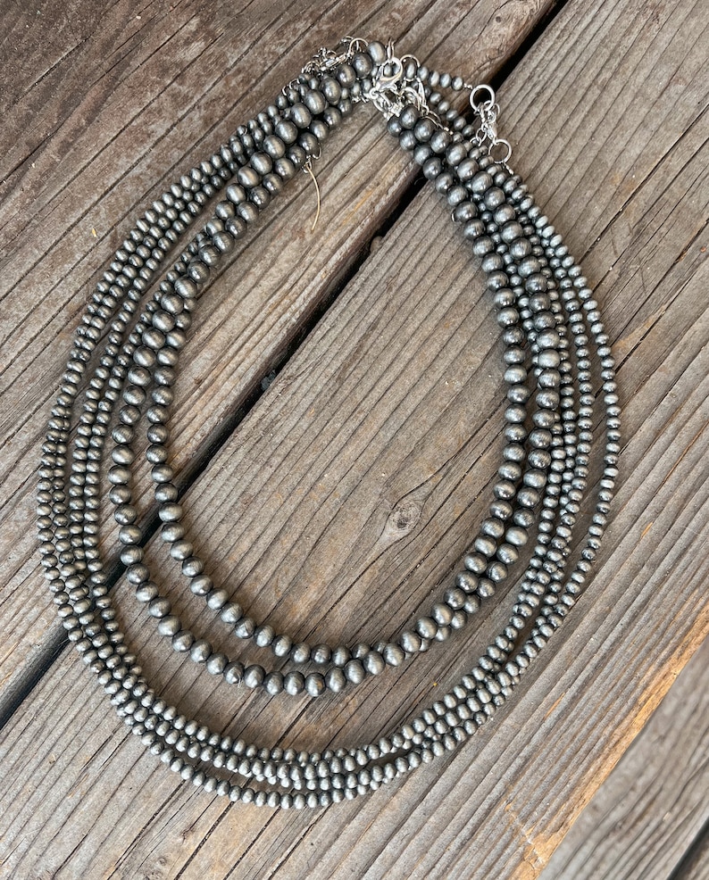 May include: A layered necklace made of five strands of gray, round, smooth beads. The necklace is made of a silver-toned metal.
