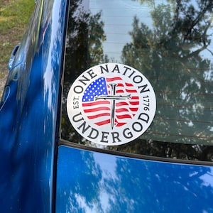 May include: A white circle sticker with the words "One Nation Under God Est. 1776" around a red, white, and blue American flag with a black cross with nails in the center.