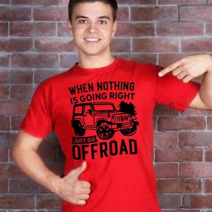 May include: Red t-shirt featuring the text "WHEN NOTHING IS GOING RIGHT JUST GO OFFROAD" and a black jeep graphic. The shirt is being worn by a person.