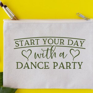May include: A white canvas makeup bag with a zipper closure. The bag has green text that reads "Start your day with a dance party" with two green hearts on either side of the word "with".