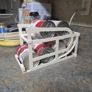 May include: White plastic can organizer with six cans of soup inside. The cans are labeled "Campbell's" and "Chicken Noodle Soup".