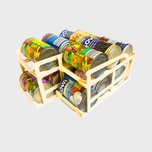 Può includere: Un organizzatore per lattine in plastica beige con più file di lattine. Le lattine sono di vari marchi e dimensioni, tra cui Latte di Cocco Goya, Fagioli Neri Goya e altri prodotti in scatola.