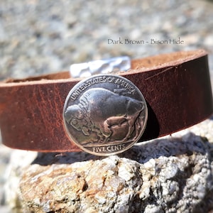 Op de afbeelding: Donkerbruine leren manchetarmband van buffelhuid met een zilveren buffelnikkel. De armband heeft een eenvoudig ontwerp met een metalen sluiting. De tekst "Dark Brown - Bison Hide" is zichtbaar.