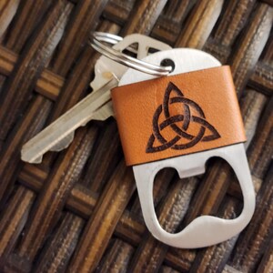 Peut inclure: Un porte-clés décapsuleur en cuir marron avec un motif de nœud celtique. Le porte-clés est doté d'un décapsuleur argenté et d'un porte-clés avec des clés attachées. L'enveloppe en cuir est de couleur marron clair.