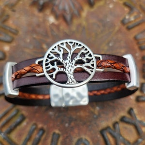 Peut inclure: Un bracelet en cuir marron avec un charm arbre de vie argenté. Le bracelet comporte un accent en cuir tressé et des fermoirs rectangulaires argentés. Le charm arbre de vie est circulaire et présente un motif découpé détaillé.
