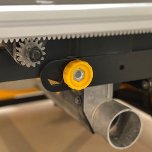 Könnte beinhalten: Nahaufnahme einer schwarzen und silbernen Tischkreissäge mit einem gelben Knopf. Die Säge verfügt über ein Getriebesystem und einen Staubabsauganschluss.