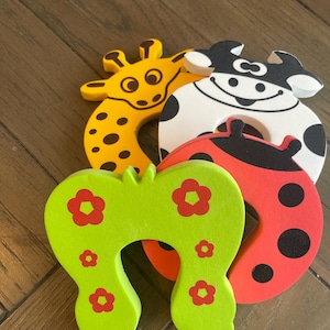 May include: Four colorful door stoppers shaped like animals. A green one with red flowers, a red one with black dots, a yellow one with brown spots, and a black and white one with black spots.