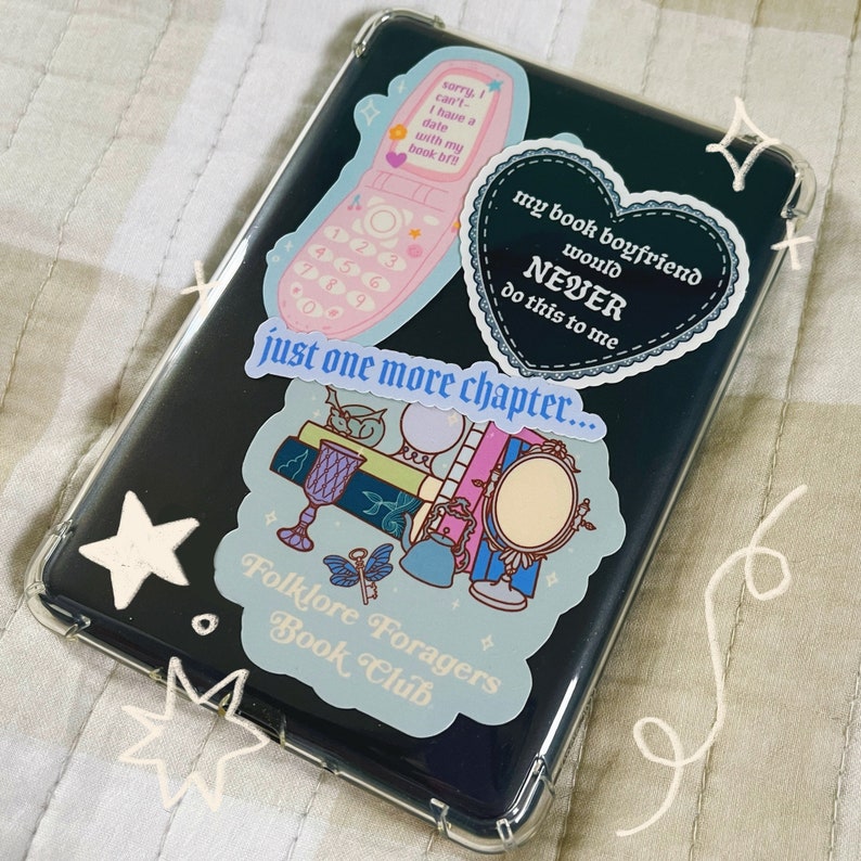 May include: A clear phone case with several stickers on it. The stickers are of a pink flip phone, a heart with the text "my book boyfriend would NEVER do this to me", a sticker with a book, a crystal ball, a mirror, and a key, and the text "just one more chapter... Folklore Foragers Book Club".