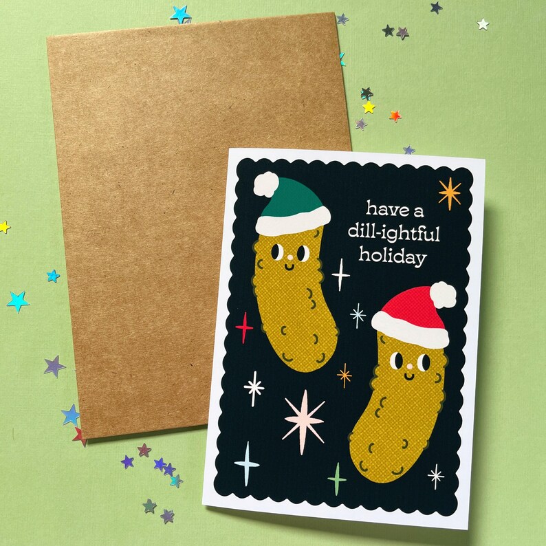 Pu&ograve; includere: Un biglietto di Natale con sfondo nero e bordo bianco a festoni. Due sottaceti di cartone animato che indossano cappelli di Babbo Natale sono sul biglietto con il testo "have a dill-ightful holiday".