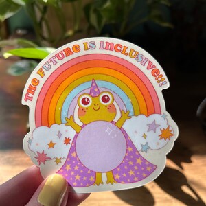 May include: A sticker with a rainbow, a frog wearing a purple cape with stars, and the text "The Future is Inclusive!!!"