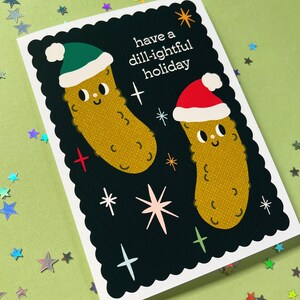 Pu&ograve; includere: Un biglietto di auguri bianco e nero con un messaggio festivo che recita "have a dill-ightful holiday". Il biglietto presenta due cetrioli di cartone animato che indossano cappelli di Babbo Natale.