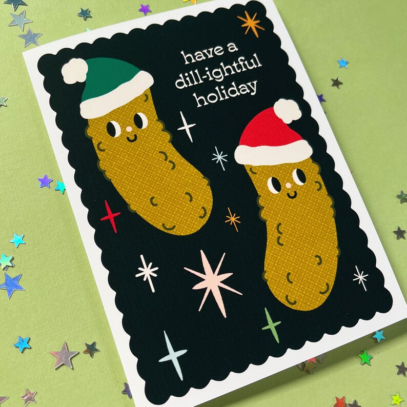 Pu&ograve; includere: Un biglietto di auguri bianco e nero con un messaggio festivo che recita "have a dill-ightful holiday". Il biglietto presenta due cetrioli di cartone animato che indossano cappelli di Babbo Natale.