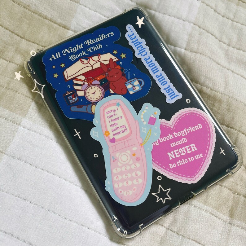 May include: A clear phone case with several colorful stickers. The stickers feature a book club logo, a pink flip phone, and a pink heart with the text "My book boyfriend would NEVER do this to me".