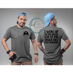 Puede incluir: Una camiseta gris jaspeada con un gráfico negro en la parte delantera que dice "HARDY" con una gorra de béisbol negra y gafas. La parte posterior de la camiseta tiene un gráfico negro que dice "Me desperté del lado equivocado de la cama del camión esta mañana."