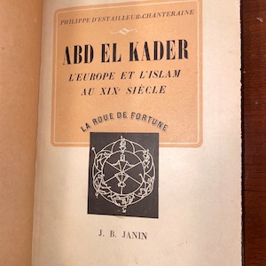 May include: A book cover with the title "Abd El Kader" and the subtitle "L'Europe et l'Islam au XIXe Siècle." The cover also features a black and white illustration of a wheel of fortune.