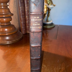 Pode incluir: Um livro encadernado em couro castanho com letras douradas na lombada. O título é "H. de Régnier - Contes Vénitiens".