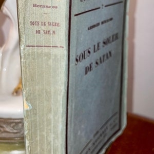 Puede incluir: Un libro vintage titulado "Le Roseau D'Or" con el texto "Oeuvres et Chroniques" y "Sous le Soleil de Satan" en la portada. El libro está encuadernado en papel azul y verde con una columna vertebral desgastada.