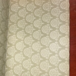 May include: A close-up of a book cover with a green background and a white repeating pattern of stylized floral designs.