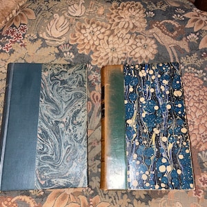 May include: Two antique hardback books with marbled covers. The book on the left has a dark blue spine and the book on the right has a dark green spine.