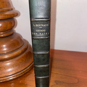 Puede incluir: Un libro encuadernado en cuero verde oscuro con letras doradas en el lomo. El título es "L. Bertrand - Le Sang Des Races".