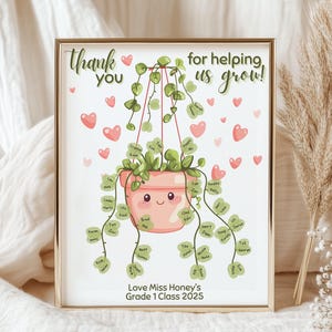 Könnte beinhalten: Ein gerahmter Druck mit goldenem Rand zeigt eine Illustration einer rosa Topfpflanze mit dem Text "Thank you for helping us grow!" und den Namen der Schüler. Rosa Herzen sind um die Pflanze verstreut. Der Text "Love Miss Honey's Grade 1 Class 2025" steht unten.