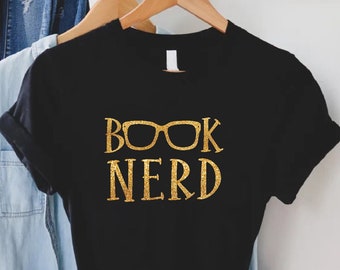 May include: Black t-shirt with gold glitter lettering that reads "BOOK NERD" with a pair of gold glitter glasses over the word "BOOK".