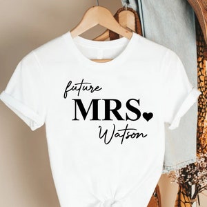 May include: White t-shirt with black text that reads "future MRS. Watson" with a small black heart.