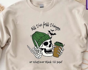 May include: Beige sweatshirt with a graphic of a skeleton wearing a green beanie and holding a coffee cup. The text reads "All the fall things" above the skeleton and "or whatever Blink-182 said" below. The sweatshirt has long sleeves.