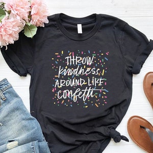 May include: Black t-shirt with the text "Throw kindness around like confetti" in white lettering and colorful confetti sprinkles surrounding the text.