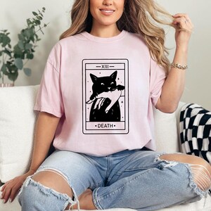 a woman sitting on a couch wearing a pink t - shirt with a black cat