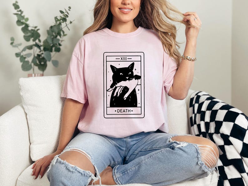 a woman sitting on a couch wearing a pink t - shirt with a black cat