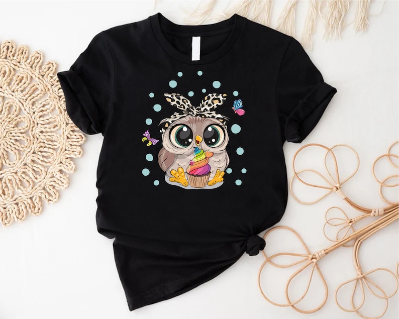 a black shirt with an owl eating a cupcake
