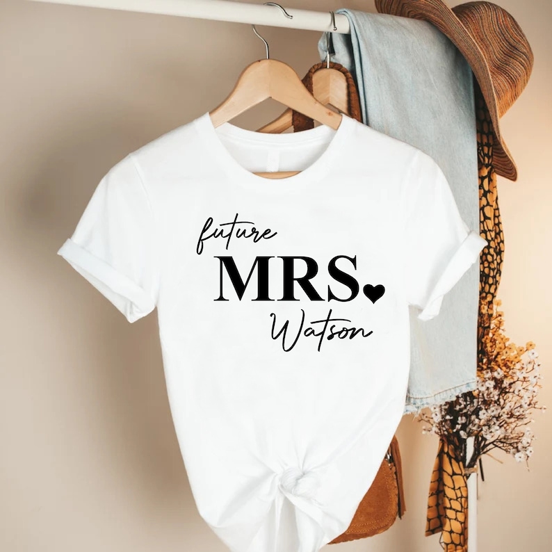 May include: White t-shirt with black text that reads "future MRS. Watson" with a small black heart.