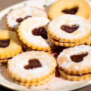 May include: A plate of homemade jam-filled cookies with a heart-shaped cutout. The cookies are dusted with powdered sugar and have a light brown color.