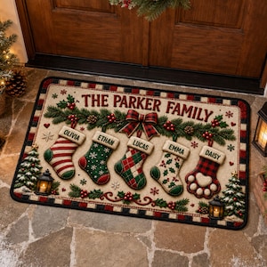 May include: A rectangular holiday doormat featuring the text THE PARKER FAMILY above five hanging stockings. The stockings are labelled Olivia, Ethan, Lucas, Emma, and Daisy, decorated with red, green, and white patterns, pine branches, and berries.