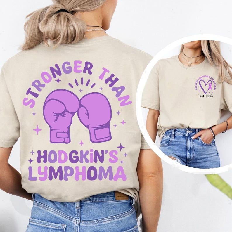 May include: Beige t-shirt with a purple graphic on the back that says "STRONGER THAN" above two purple boxing gloves and "HODGKIN'S LYMPHOMA" below. A smaller graphic on the front shows a heart with a purple ribbon and the words "HODGKIN'S LYMPHOMA AWARENESS" and "Team Linda."