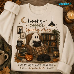 May include: A cream-coloured sweatshirt featuring a graphic of a ghost sitting in an armchair reading a book. The text reads: books coffee spooky vibes and JUST ONE MORE CHAPTER before bed. Includes illustrations of a black cat, pumpkins, and a bookshelf.