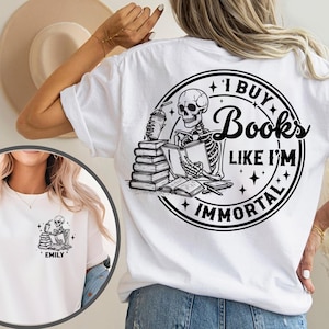 Peut inclure: T-shirt blanc avec un motif noir d'un squelette lisant des livres et tenant une boisson. Le texte sur le t-shirt dit "I BUY BOOKS LIKE I'M IMMORTAL". Une version plus petite du motif est sur le devant.