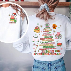 May include: White sweatshirt with a colorful graphic on the front and back. The front features a stack of rings with a Santa hat. The back has a list of physical therapy milestones and the text "12 Days of Physical Therapy".