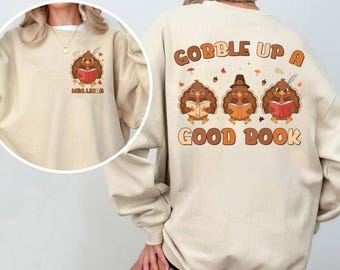 May include: Beige sweatshirt featuring a cartoon turkey reading a book, with the text "Mrs. Linda" on the front. The back displays three turkeys reading books with the text "Gobble Up A Good Book". The design includes fall leaves and a pilgrim hat.