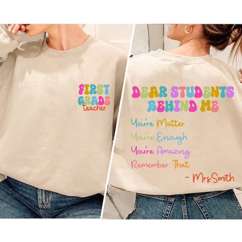 May include: A beige sweatshirt with the text "FIRST GRADE teacher" on the front and "DEAR STUDENTS BEHIND ME You're Matter You're Enough You're Amazing Remember That - Mrs. Smith" on the back.