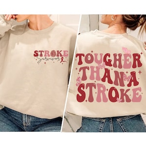 May include: A beige sweatshirt with the text "STROKE Survivor" on the front and "TOUGHER THAN A STROKE" on the back. The text is in a retro font with pink and red accents. There are butterflies on the back of the sweatshirt.